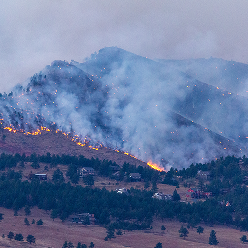 A wildfire rages, with homes seen in the foreground.