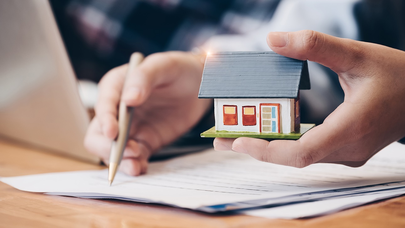 Person filing paperwork and holding a tiny house