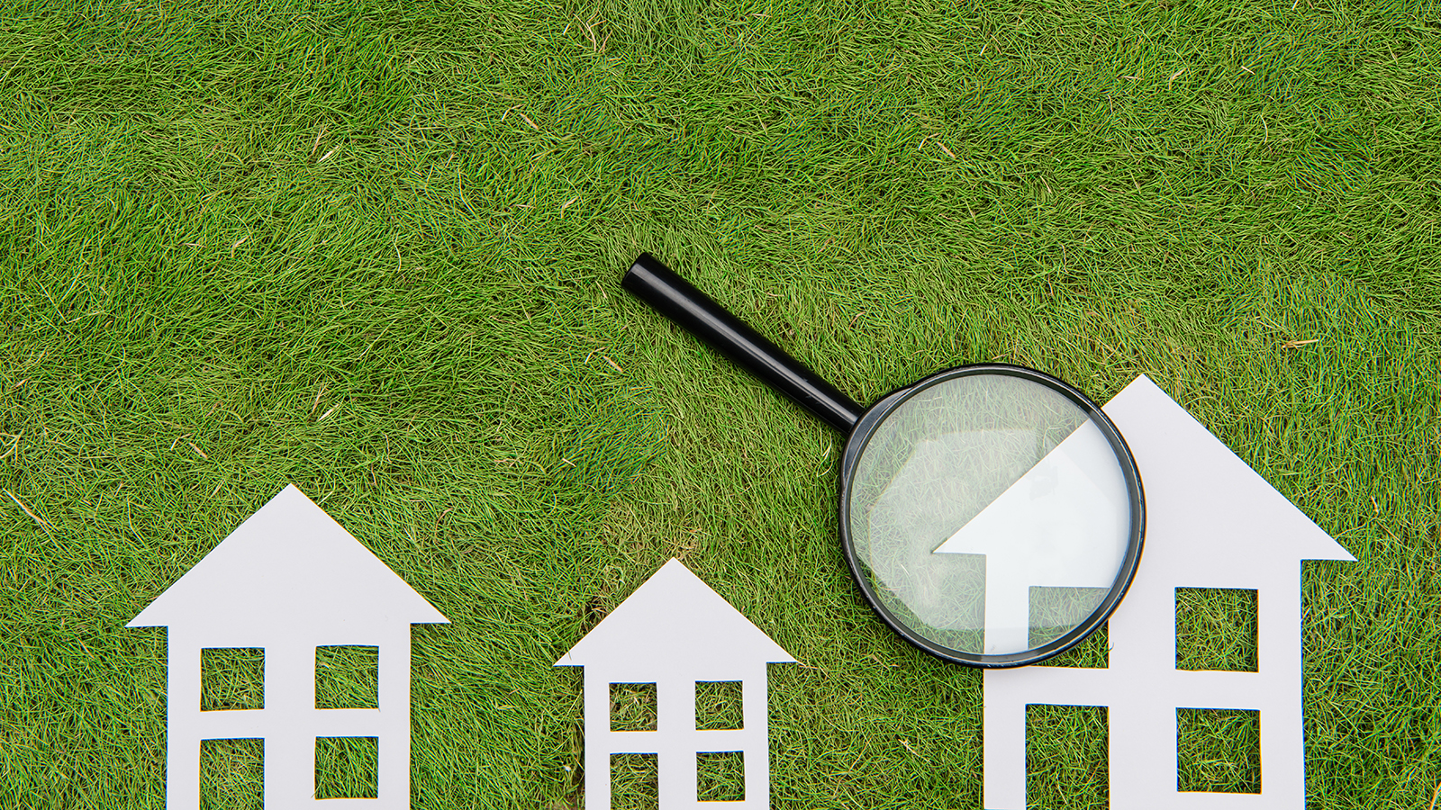 Three paper houses with a magnifying glass on one of them