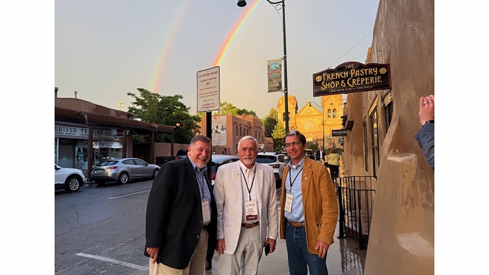 three individuals on sidewalk in front of double rainbow