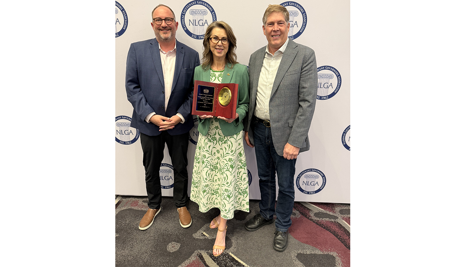 three people standing and person with award in the middle