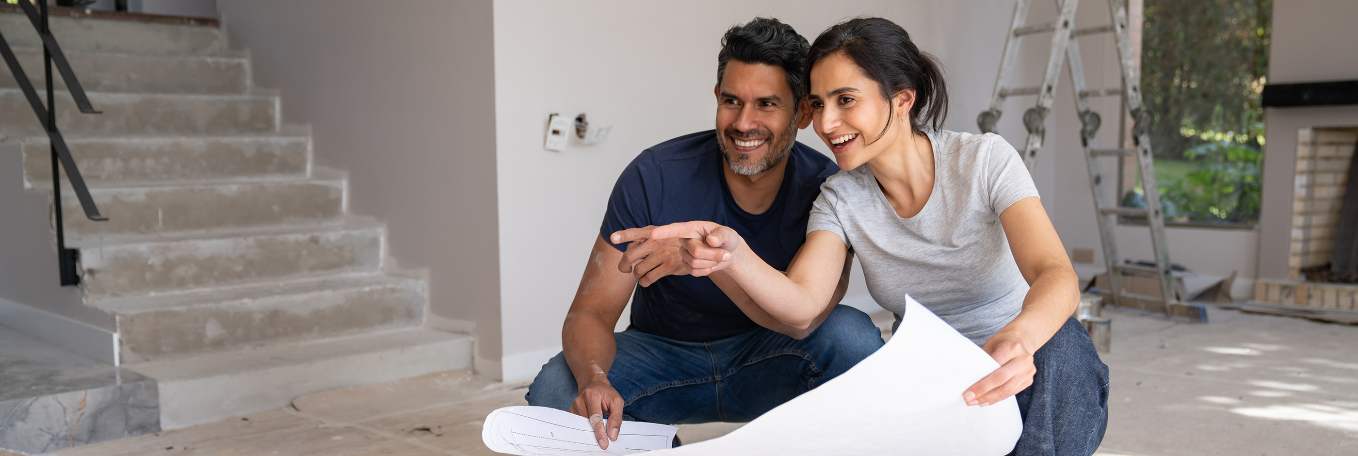 Loving Latin American couple remodeling their house and pointing away while looking at a blueprint
