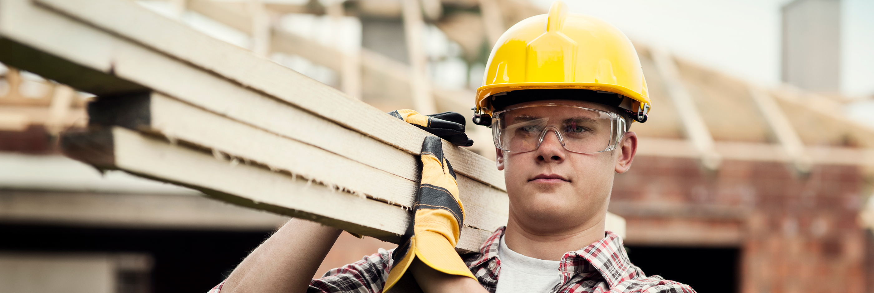 Construction worker carrying wood with proper gloves and hat