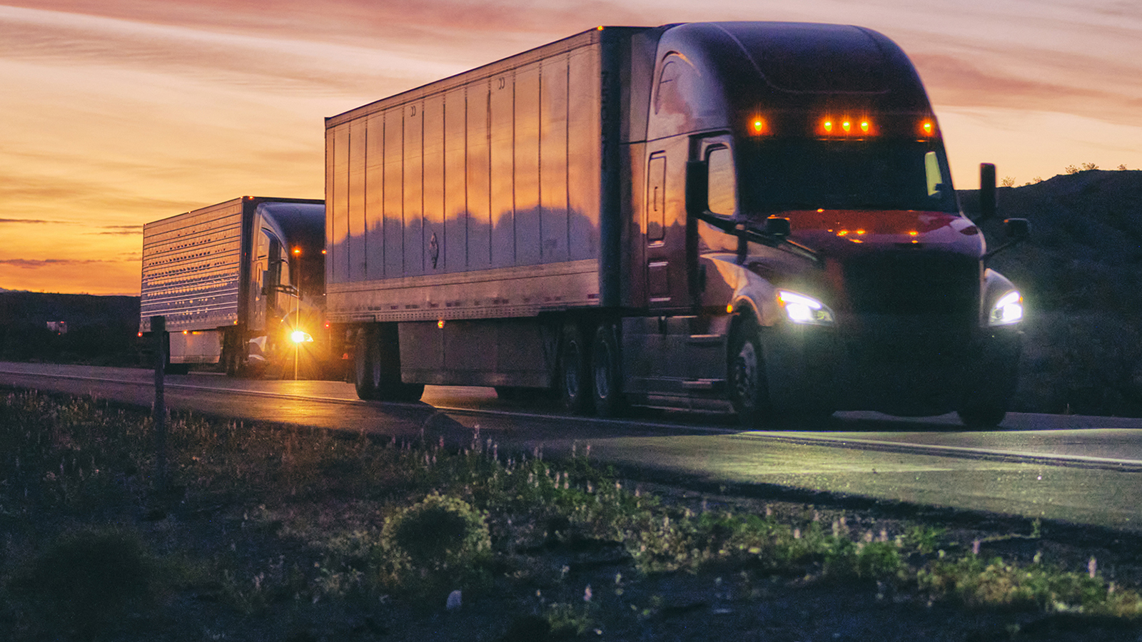 Two Semi-trailer trucks driving in the sunset