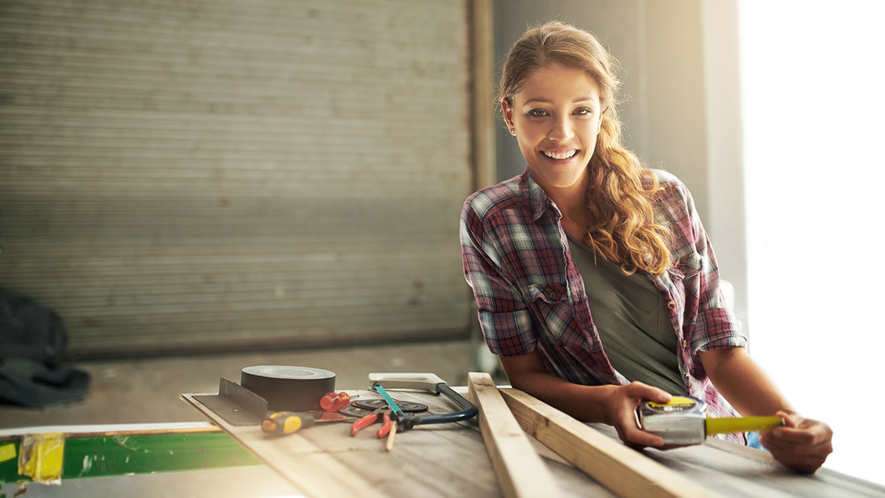 Woman holding a measuring tape around carpentry equipment