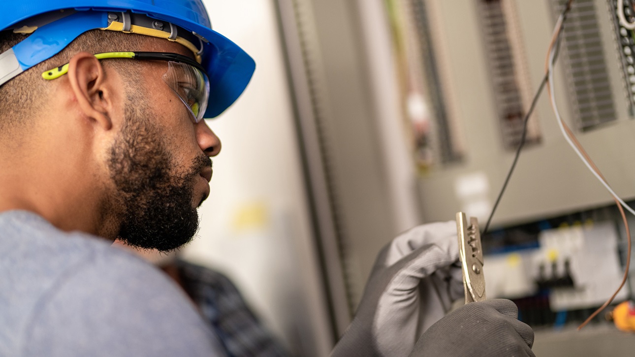 An electrician cutting a wire in front of a circuit box