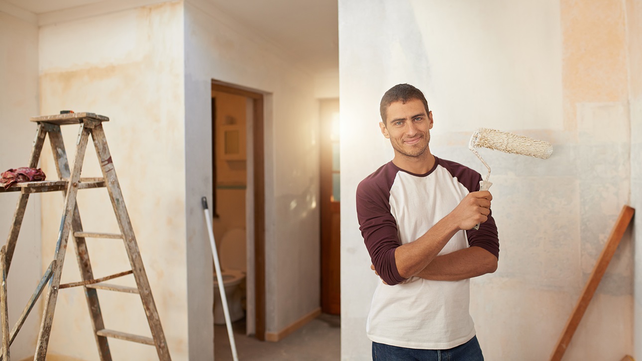 Man holding roller brush in a room half painted