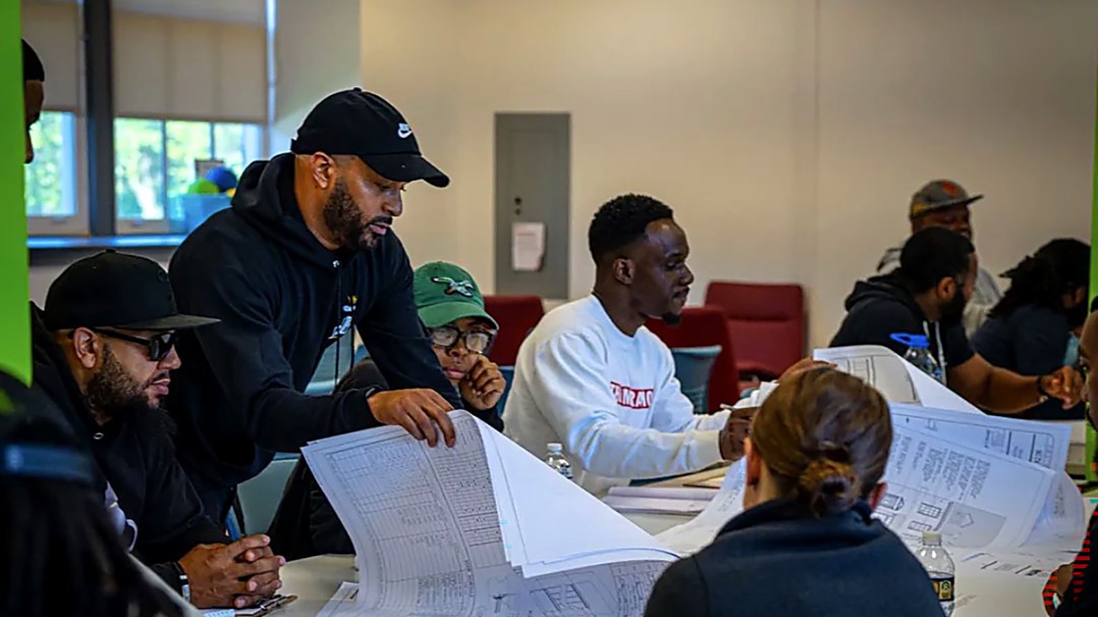 Jordan Parisse-Ferrarini stands and guides students seated at a table.