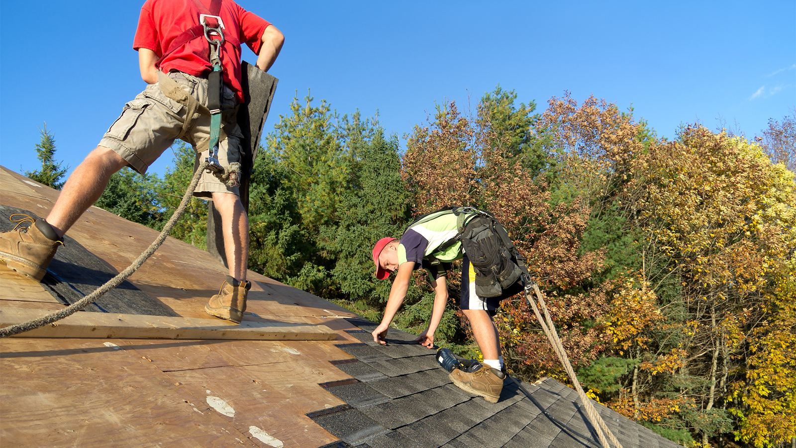 Two men working on a roof with fall protection harnesses