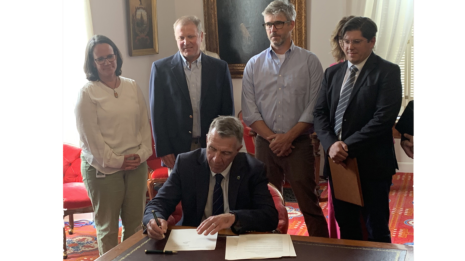 governor at desk signing with individuals 