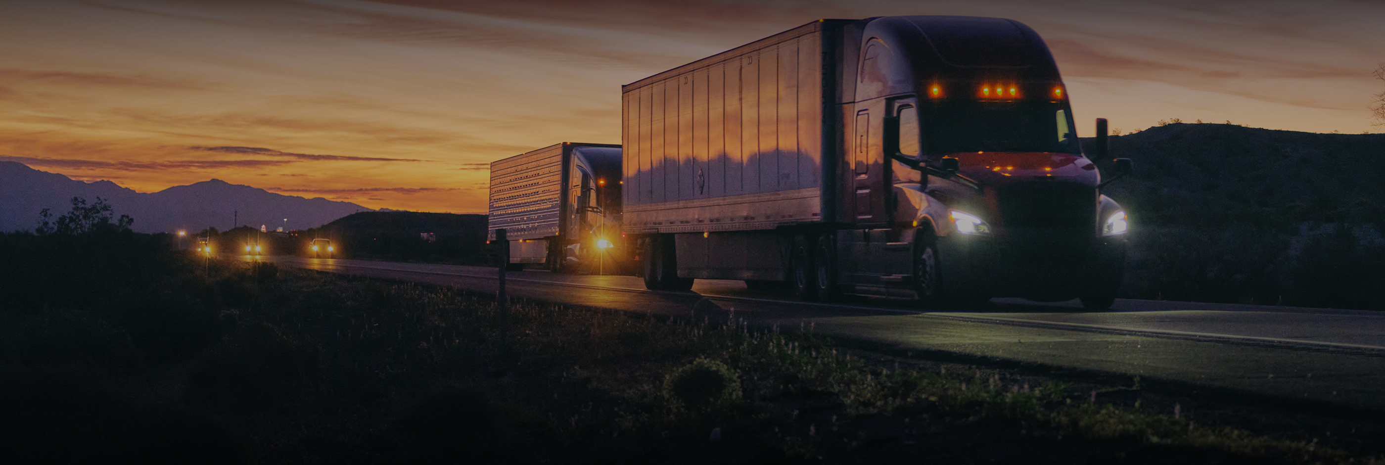 Two Semi-trailer trucks driving in the sunset