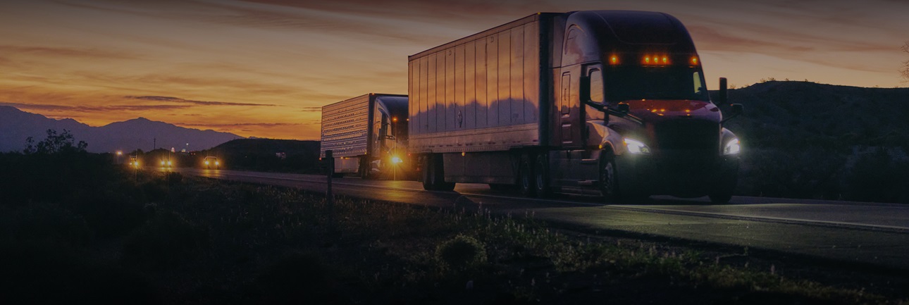 Two Semi-trailer trucks driving in the sunset