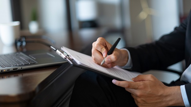 Man sitting in an office holding pen writing in a notebook
