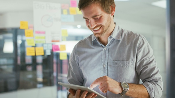 A man smiling while looking at a tablet and sticky notes around
